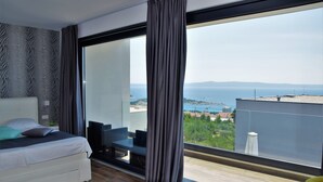 Una moderna camera d'albergo con un letto grande, un balcone vista mare e un'area pranzo con mobili da esterno.
