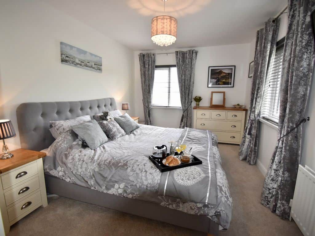 Un dormitorio con una cama grande, una mesita de noche, un aparador, una ventana con cortinas y un candelabro.