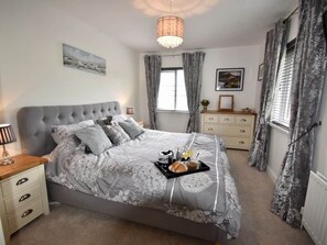 A bedroom with a large bed, a bedside table, a dresser, a window with curtains, and a chandelier. - Beachfront, Antrim Coast, Stunning Views & Hot Tub (Glenarm)
