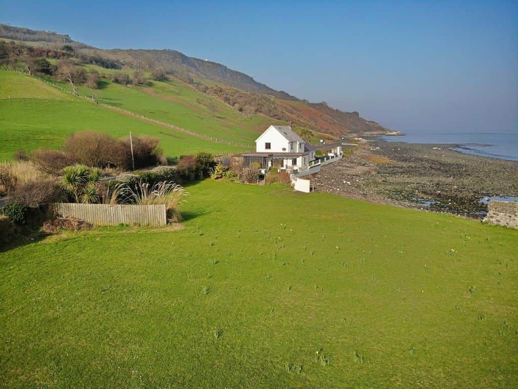 A coastal property with a white house, a grassy lawn, and a rocky shoreline.