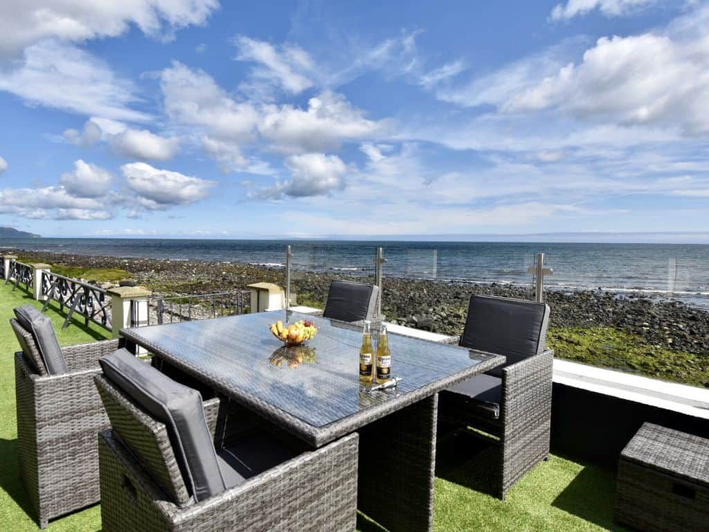 An outdoor dining area with a table and chairs, overlooking a rocky coastline and the sea.