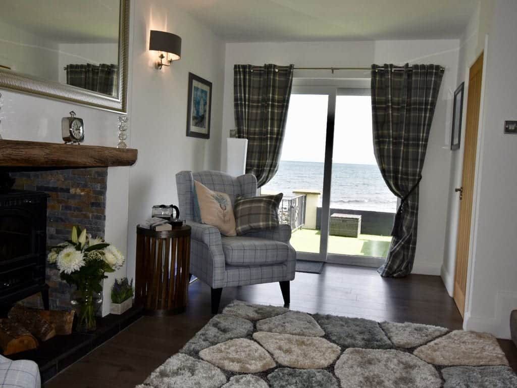 A living room with a fireplace, a sofa, a rug, and a view of the sea through curtains.