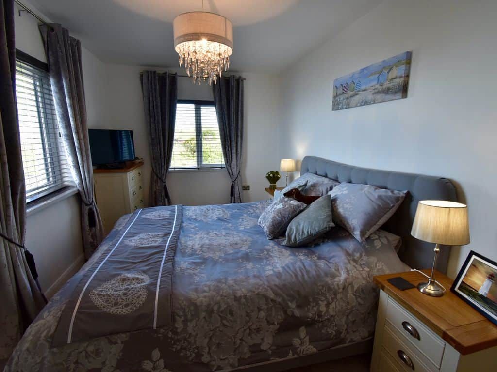 A bedroom with a bed, bedside lamps, a television, and a painting on the wall.
