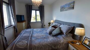 A bedroom with a bed, bedside lamps, a television, and a painting on the wall.