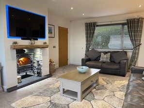 A living room with a fireplace, a sofa, a coffee table, and a television mounted on the wall. - Beachfront, Antrim Coast, Stunning Views & Hot Tub (Glenarm)