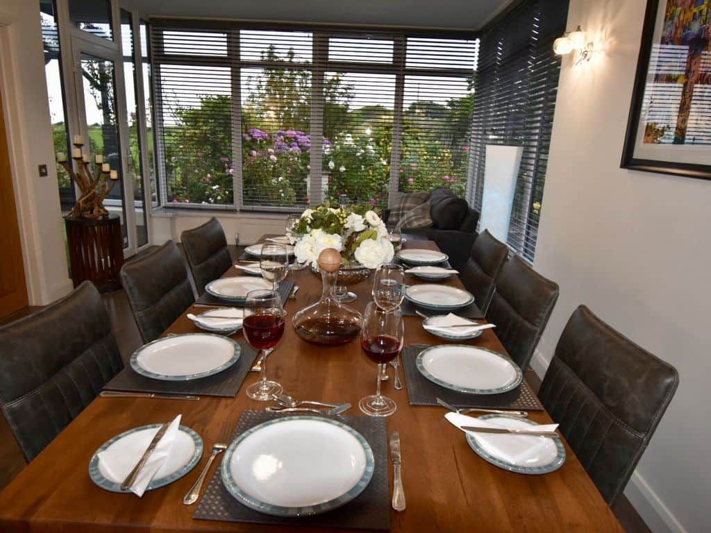 A dining table set for 8 with a view of the garden through large windows.