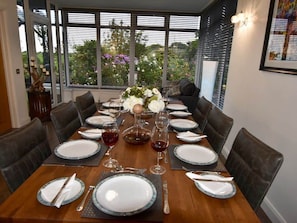 Une table à manger dressée pour huit personnes, avec vue sur le jardin grâce à de grandes fenêtres.