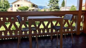 Un balcon avec une table et deux chaises, donnant sur un jardin et une maison.