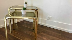 Une petite table d’angle avec un plateau en verre et des pieds dorés, agrémentée d’une petite plante en pot.