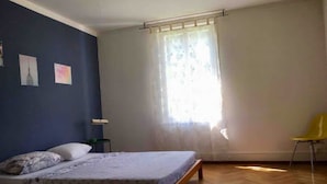 Une chambre à coucher avec un lit, une chaise, une table de chevet et une fenêtre avec des rideaux.