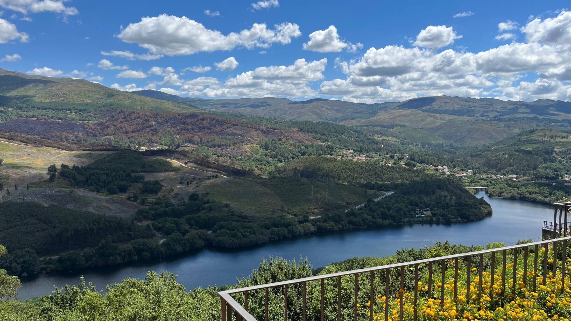 A panoramic view of a valley with a lake, surrounded by hills and a clear sky.