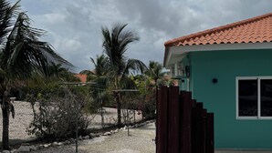 Una casa con fachada verde y tejado de tejas rojas, rodeada de grava y palmeras.