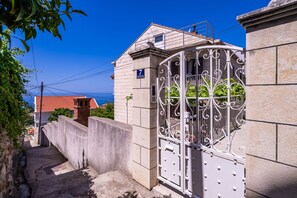 Traditional building with a pitched roof and balcony, featuring a secure wrought iron gate and a narrow pathway to the entrance.