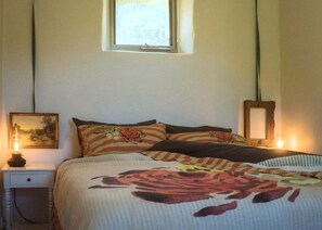 Un dormitorio con una cama, dos lámparas de noche, un ventanal y un cuadro en la pared.