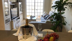 Un salon moderne avec un canapé, une table à manger ornée d’une bouteille de champagne, d’un verre et d’une assiette de fruits.