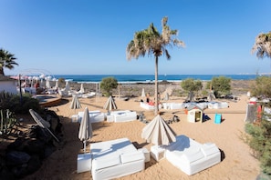 A beach with white lounge chairs and umbrellas, a palm tree, and a rocky shoreline. - Palmar dreams great duplex- penthouse in Tenerife (Arona)