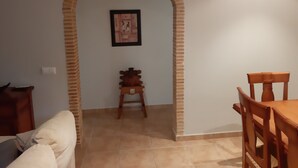 Een eetgedeelte met een houten tafel en stoelen, een klein krukje en een lijst met een afbeelding aan de muur.