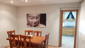 Een eethoek met een houten tafel en stoelen, een aan de muur bevestigd Boeddha-kunstwerk, en een keuken die zichtbaar is door een open doorgang.
