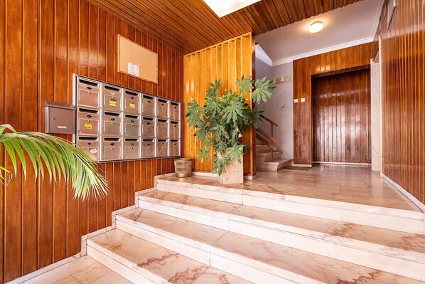 A wooden interior with a set of mailboxes, a potted plant, and a staircase leading to a door.