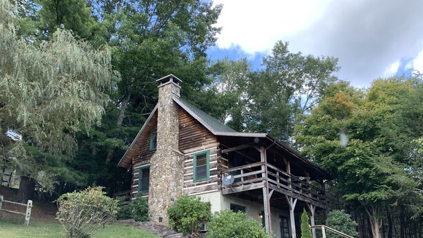 A log cabin with a stone chimney, a balcony, and a stone foundation.