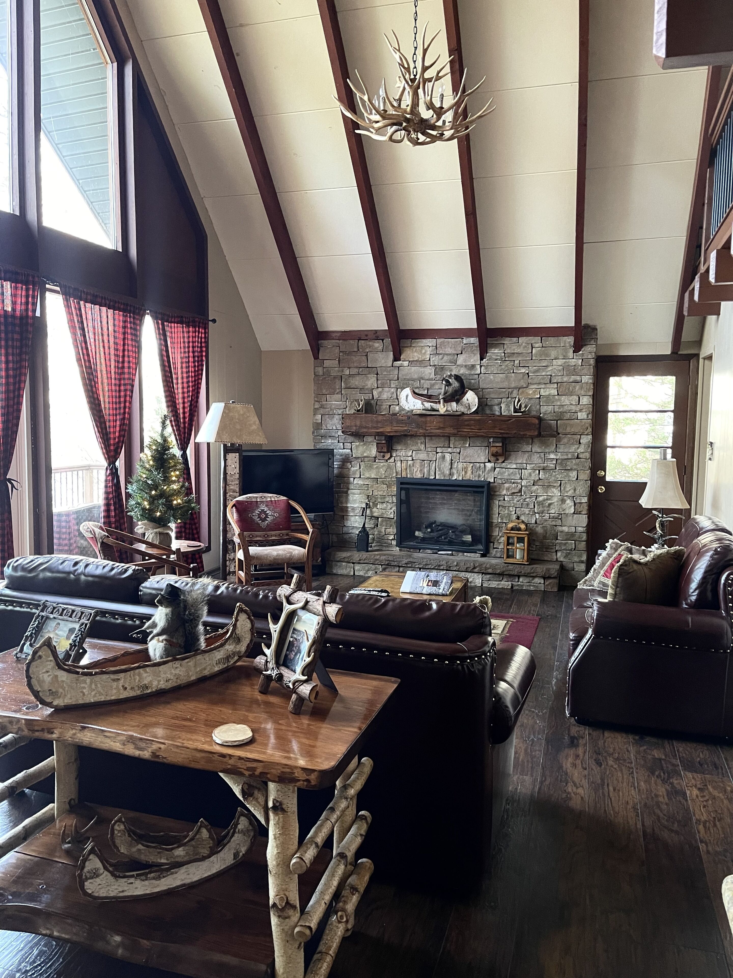 A cozy living room with a stone fireplace, leather furniture, and a Christmas tree.