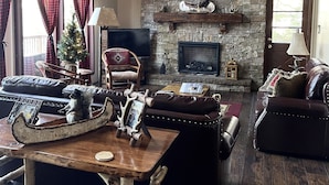 Una sala de estar acogedora con chimenea de piedra, muebles de cuero y un árbol de Navidad.