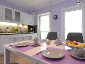 A modern kitchen with white cabinets, a dining table set with plates, cups, and a bowl of fruit. - Tide App. 4 dike light (Ostseebad Boltenhagen)
