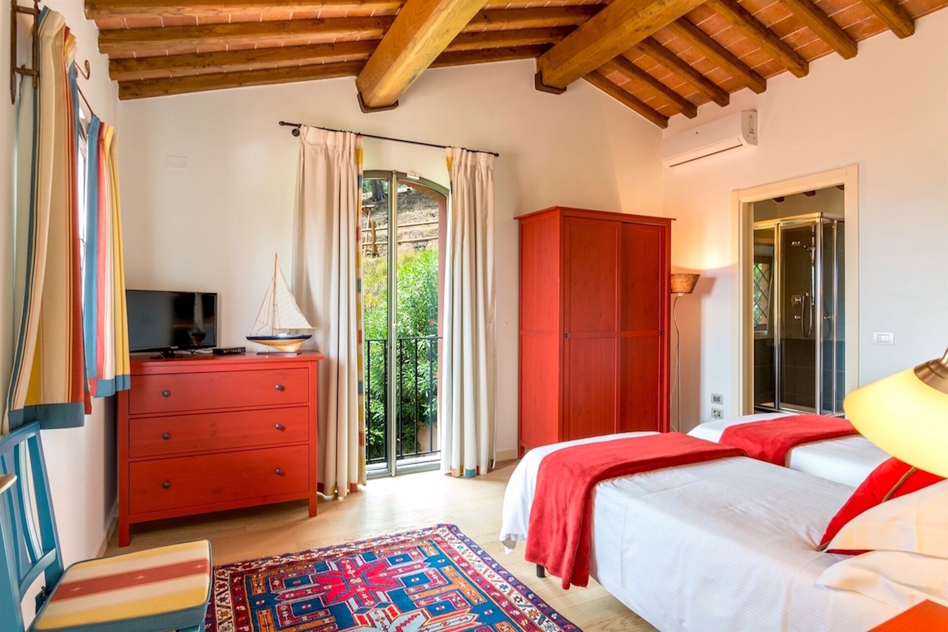 A bedroom with a bed, a dresser, a TV, a wardrobe, and a balcony with curtains.