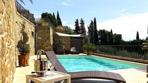 Un área de piscina con una silla de descanso, una mesa con una bebida y un muro de piedra.