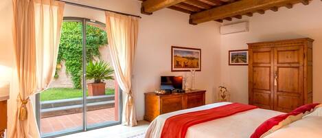 Un dormitorio con una cama, un armario de madera, un televisor sobre un mueble de madera y un ventanal corredero que da a un jardín.