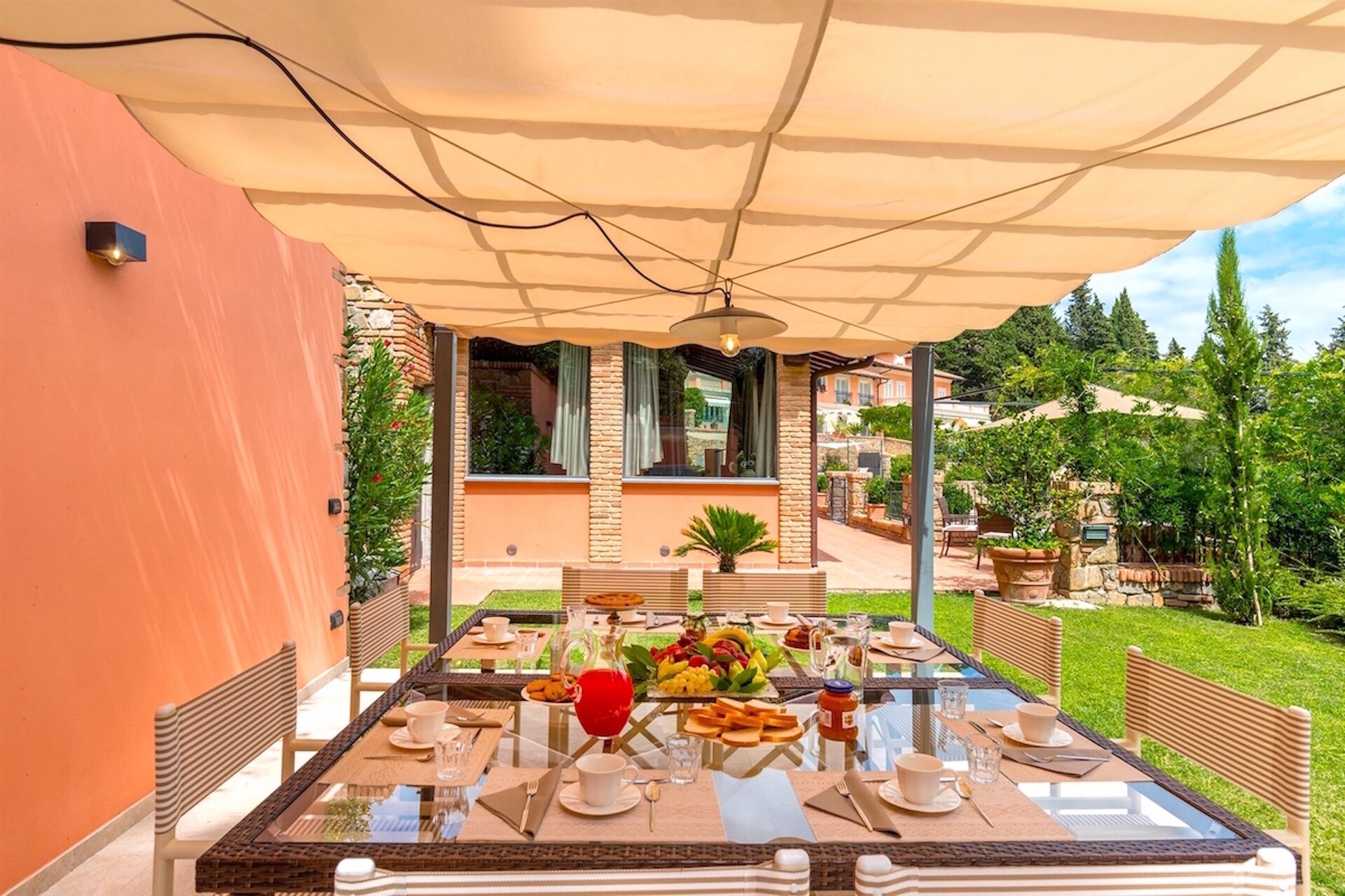 Un tavolo da pranzo all'aperto con piano in vetro, circondato da sedie e ombreggiato da un grande ombrellone.