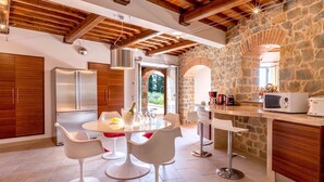 Una cocina moderna con pared de piedra, vigas de madera y comedor con sillas blancas.