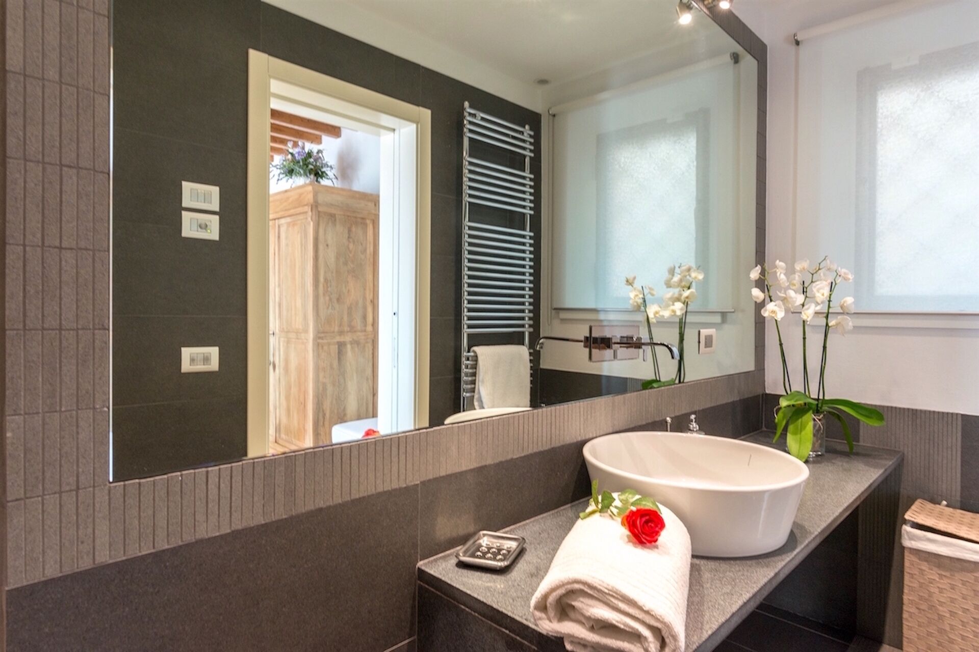 A modern bathroom with a large mirror, a white sink, a towel, and a small tray.