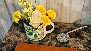 A brown leather notebook with "Guests" embossed on the cover, a mug with a floral design, and a decorative spoon on a granite countertop.