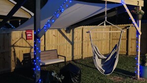 A covered outdoor area with a hammock, a bench, and a potted plant.
