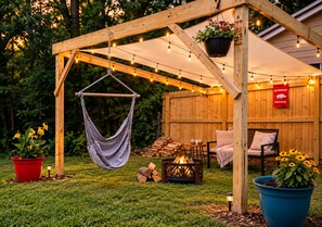 A wooden pergola with string lights, a hanging chair, a fire pit, and outdoor seating. - The Cozy King Studio #2 (Benton)