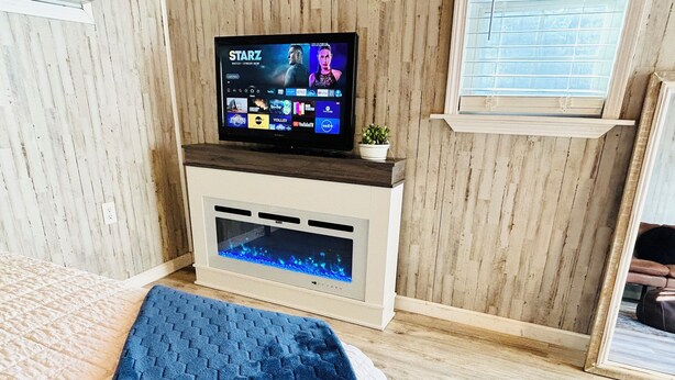 A room with a bed, a TV on a wooden shelf, a small plant, and a built-in aquarium.