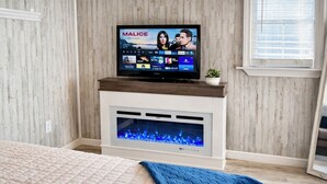 A modern living room with a fireplace, a television displaying a show, and a bed with a quilt.