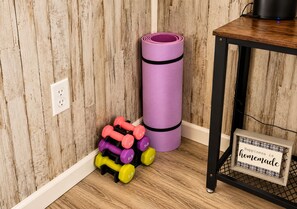 A corner of a room with a wooden floor, a purple exercise mat, and a set of dumbbells. - The Cozy King Studio #2 (Benton)