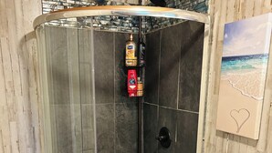 A corner shower with a glass enclosure, a built-in shelf with toiletries, and a beach-themed artwork on the wall.