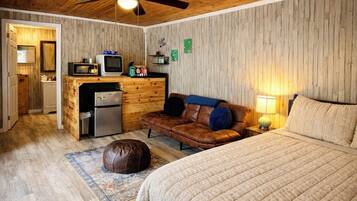 Una habitación acogedora con una cama, un sofá de cuero marrón, una kitchenette pequeña y un ventilador de techo.