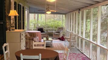Une véranda abritée avec une table et des chaises, un ventilateur de plafond et une vue sur la verdure environnante.