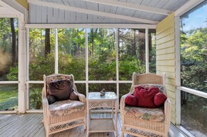 A covered porch with wicker furniture and a view of a forested area.