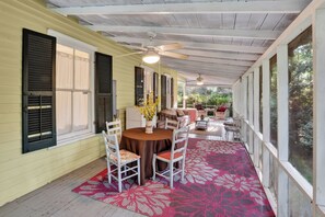 A covered porch with a dining table, chairs, and a red floral rug.