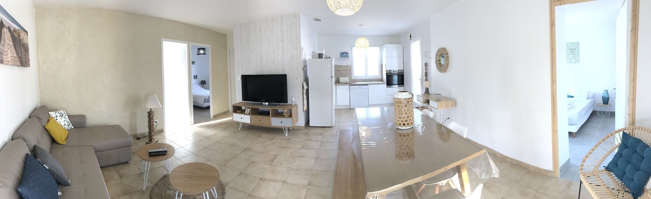 A modern living room with a sofa, coffee table, and TV. A kitchen is visible in the background with a refrigerator and cabinets.