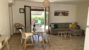 A living room with a sofa, a dining table, and a chair. There is a painting on the wall and a clock. - Renovated house, 300m from the beach, with a boule court (La Brée-les-Bains)