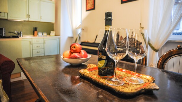 Una mesa de comedor con una botella de vino, dos copas de vino y un cuenco de fruta.