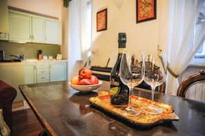 Une table à manger avec une bouteille de vin, deux verres à vin et un saladier de fruits.