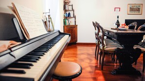 Un piano con partituras, una estantería y un comedor con sillas y una mesa.