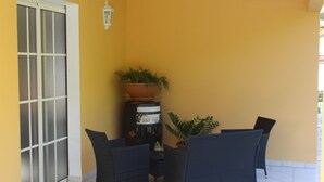 Een terras met een hoekje, twee rieten stoelen, een tafeltje, een bloempot en een decoratieve vat.